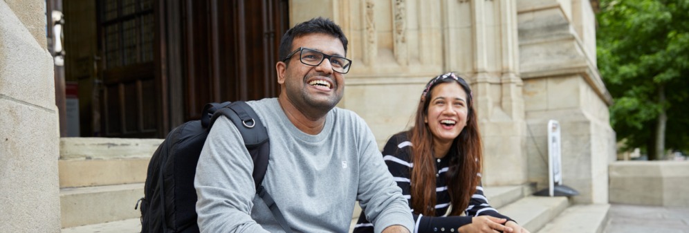 Two postgrad students, a male and female, sitting on the steps outside the Wills Memorial Building, looking towards the camera, laughing.